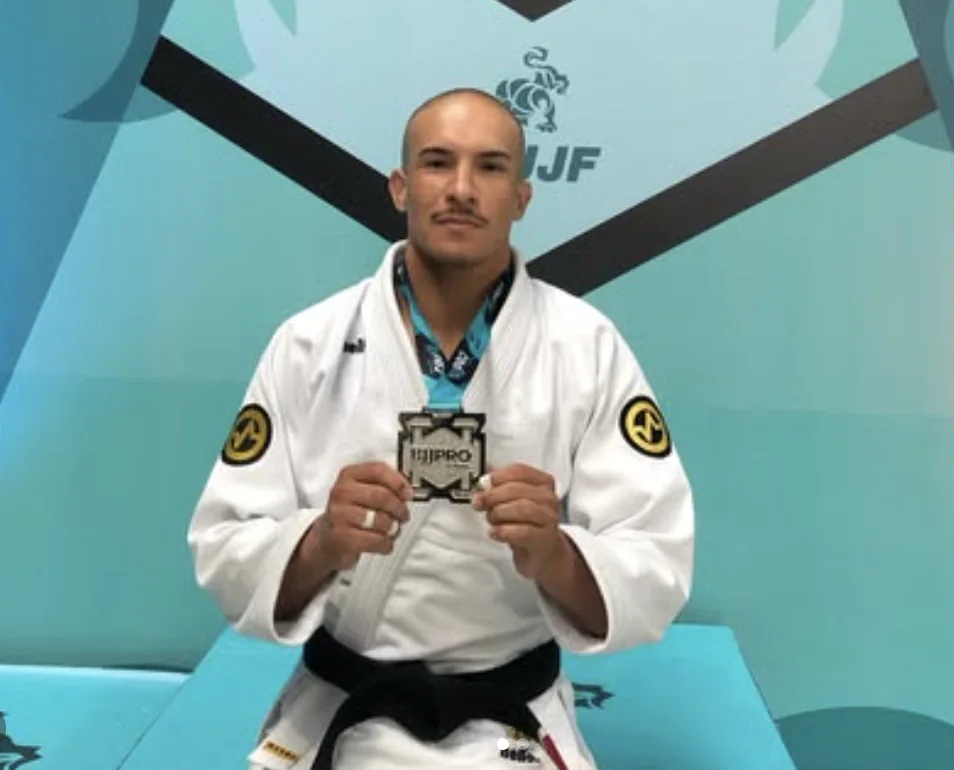Guilherme Coelho de kimono e faixa preta segurando uma medalha de campeonato de jiu-jítsu